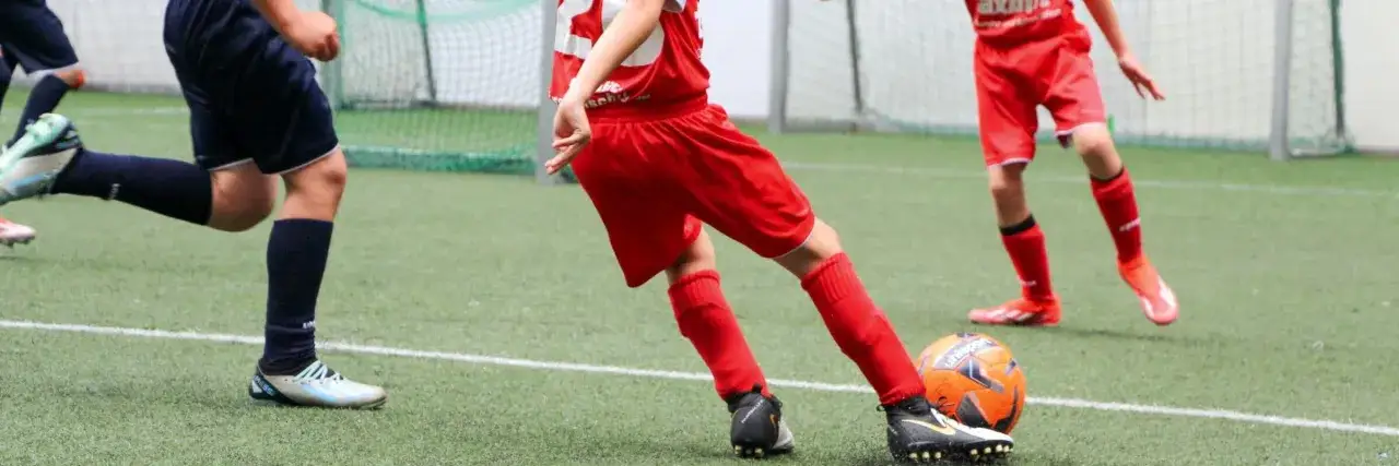 Kinder im Fußballtraining üben das Passen. Ein Ball liegt auf dem Kunstrasen, die Beine der jungen Spieler sind in Aktion.