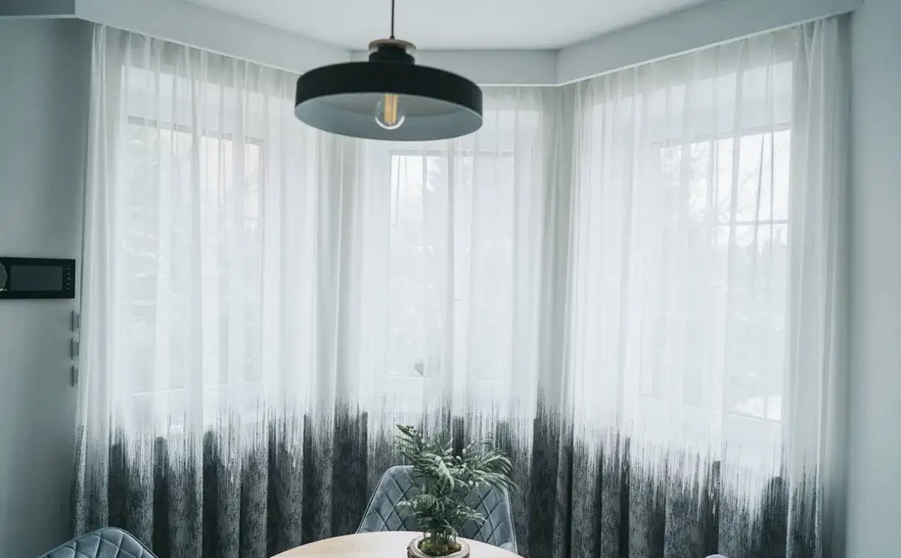 Eleganckie firanki w wykuszu, z nowoczesnym wzorem, dodają wnętrzu lekkości. Montaż na karniszu szynowym ułatwia ich przesuwanie.