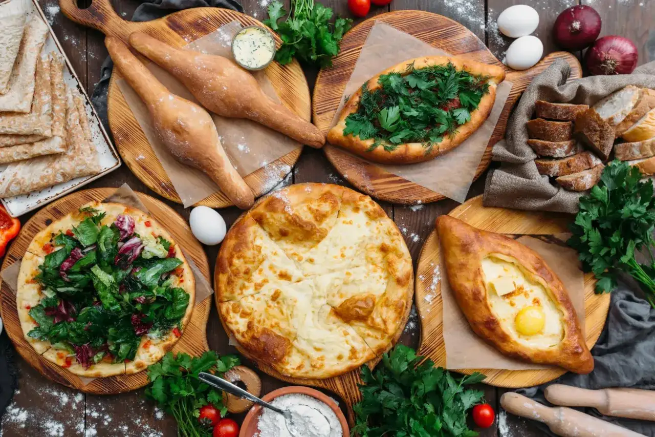 Gruzińskie pierogi i chaczapuri na drewnianych deskach, z ziołami, jajkami i pieczywem.