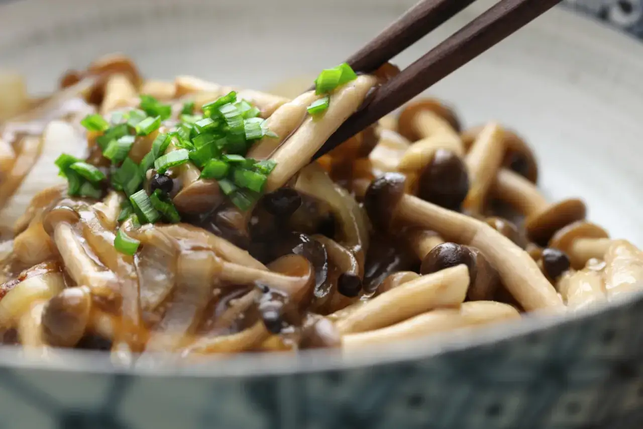 Chopsticks podnoszą pyszne grzyby shimeji w sosie, posypane szczypiorkiem.