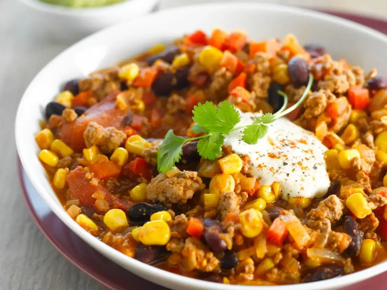Herzhaftes Chili sin Carne mit Bohnen, Mais und Hackfleisch, garniert mit einem Klecks Sauerrahm und Koriander.