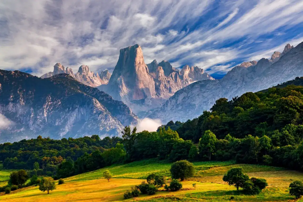 Majestatyczne szczyty Picos de Europa wznoszą się nad zielonymi dolinami i lasami, a niebo zdobią malownicze chmury.