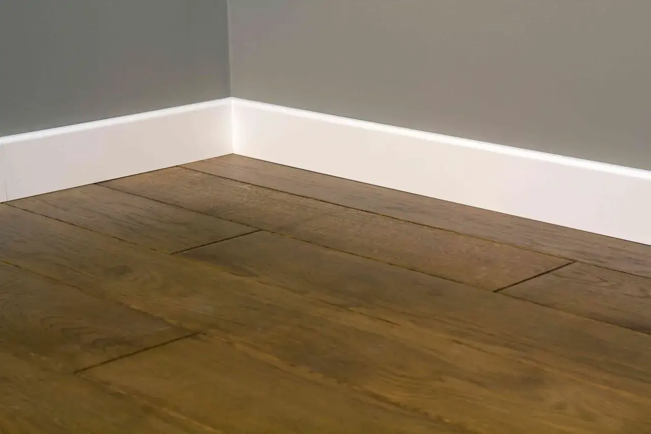 Esquina de una habitaci&oacute;n con suelo de madera oscura y rodapi&eacute;s blancos, igual que las puertas o que el suelo.