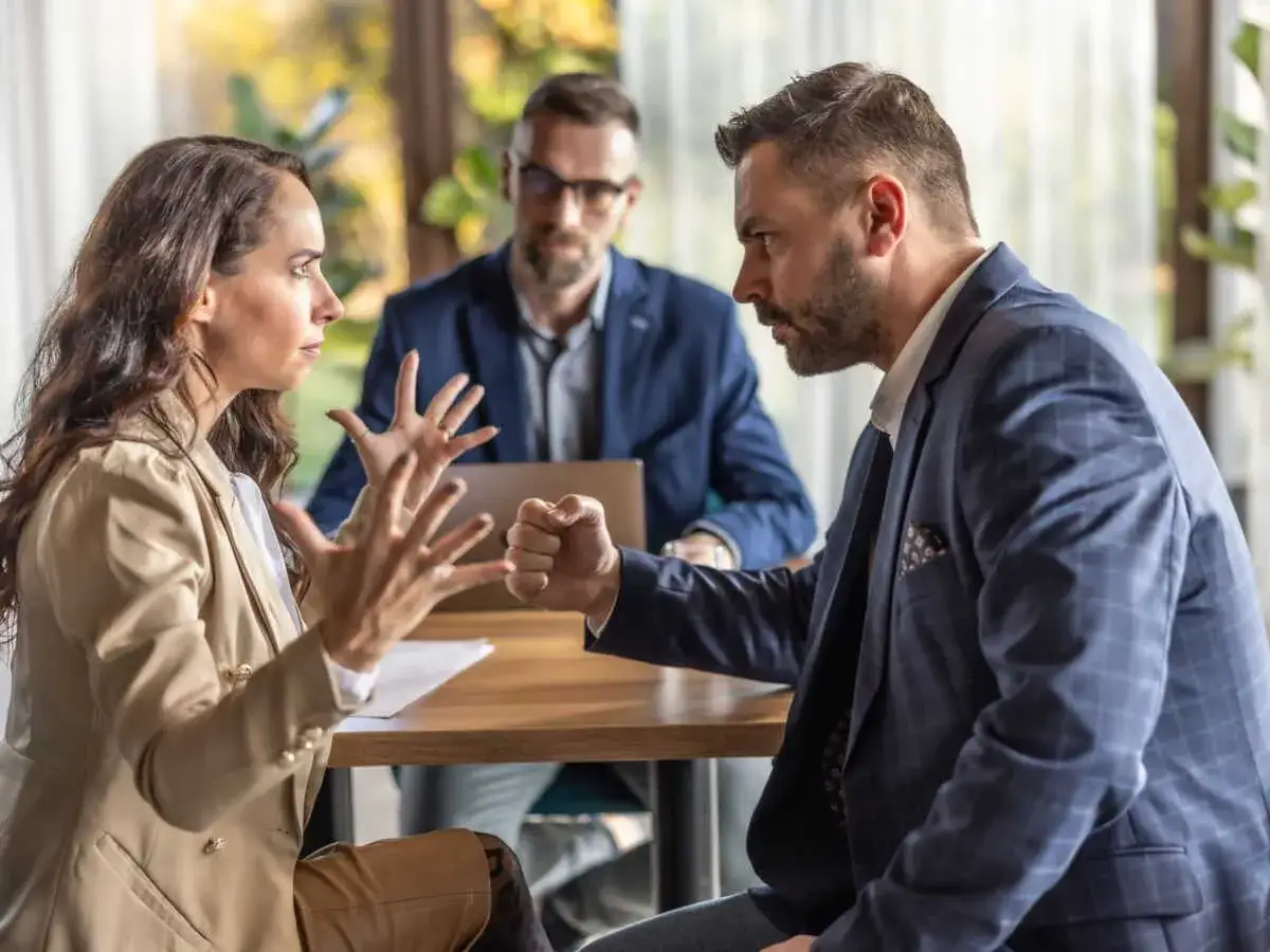 Un couple en pleine discussion tendue, possiblement lors d'une consultation pour une aide juridictionnelle dans le cadre d'un divorce. Un homme écoute attentivement.