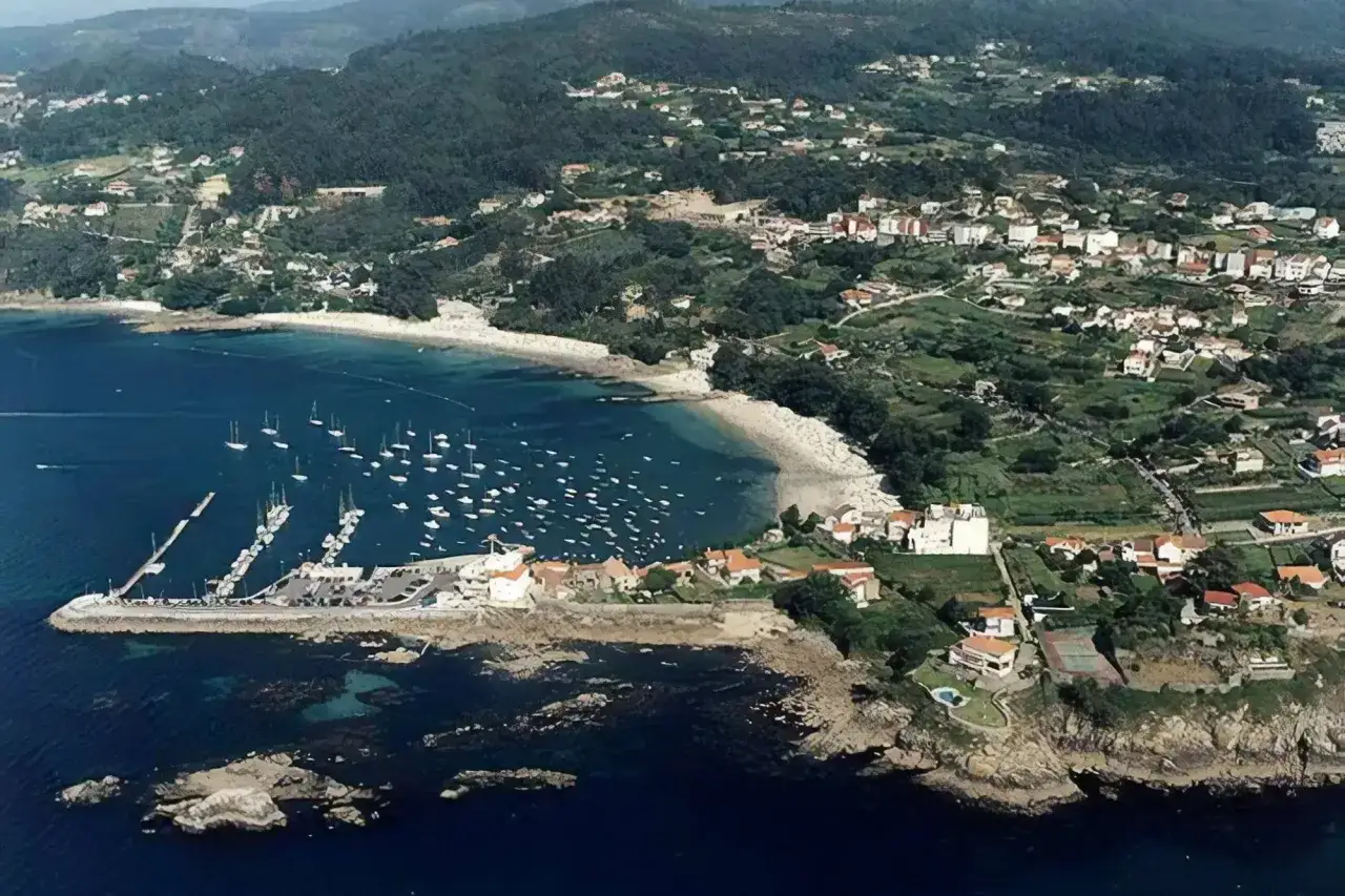 Vista aérea de la **playa de Aguete** con un puerto deportivo lleno de veleros, casas blancas y verdes colinas.