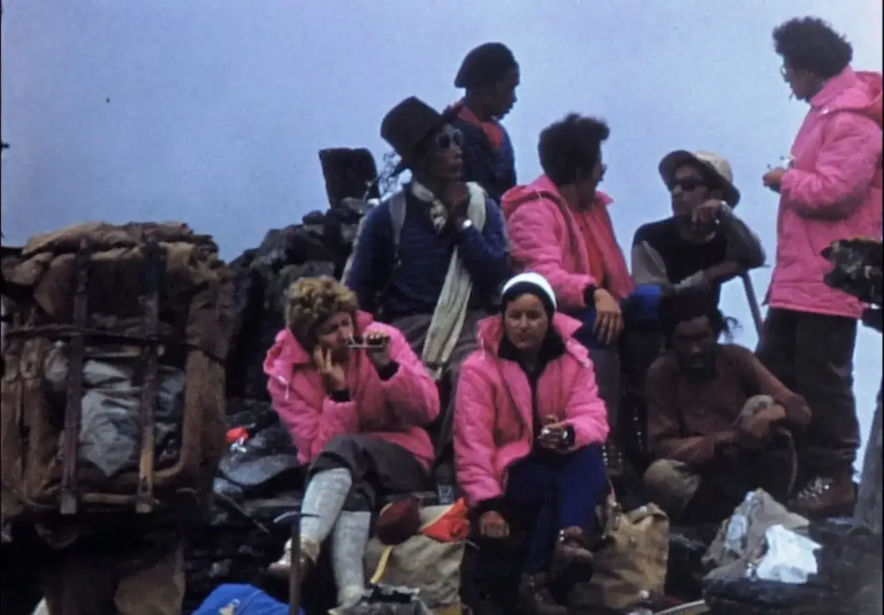 Groupe de randonneurs, dont Claude Kogan, se reposant sur un flanc de montagne, vêtus de vestes roses vives.