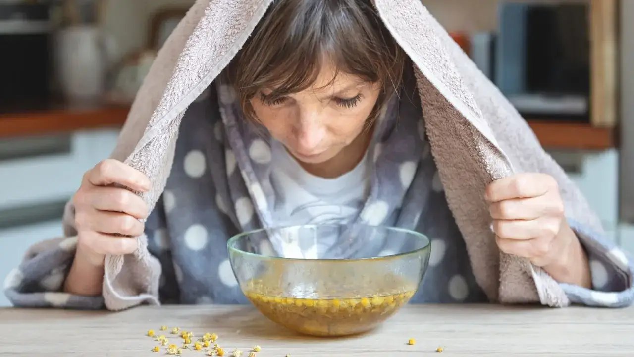 Frau inhaliert Dampf aus Kamillentee. Eine gute Idee, was essen bei Grippe, um sich zu erholen.