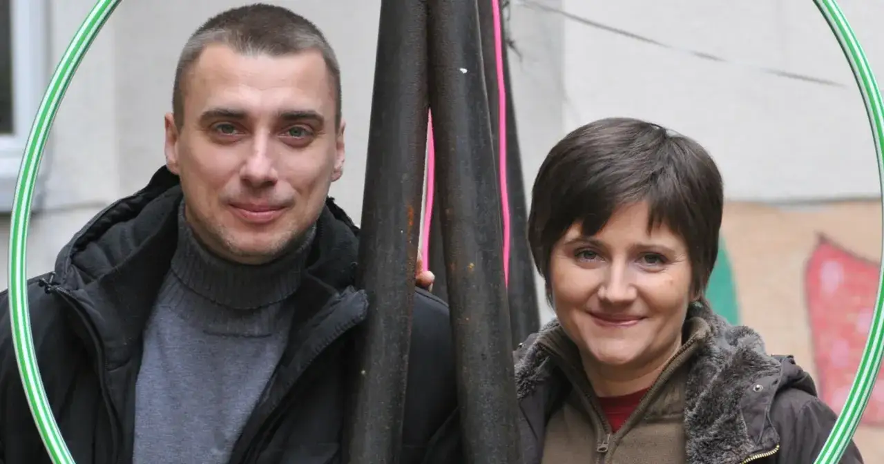 Maciej Dębosz prywatnie z uśmiechniętą kobietą, otoczeni zieloną obręczą i metalowymi rurami.