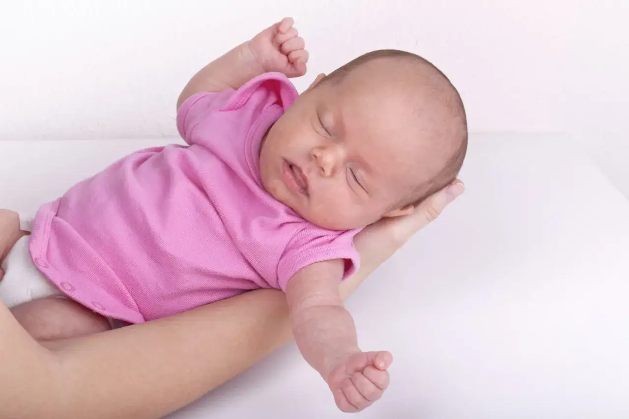 Neonato in rosa si irrigidisce e stringe i pugni, dormendo serenamente tra le braccia.