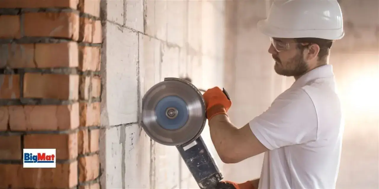 Obrero con equipo de protecci&oacute;n usa una amoladora angular, una de las herramientas de medici&oacute;n y corte, para trabajar en una pared de ladrillos y bloques.