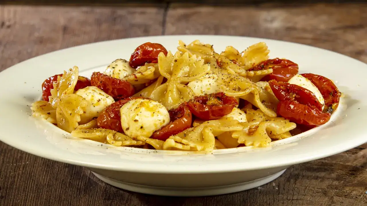 Farfalle con pomodorini confit, mozzarelline e un tocco di acciughe per un sapore mediterraneo.
