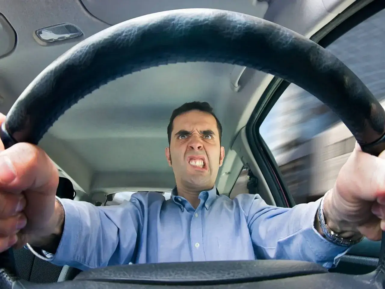 Uomo con espressione di forte ansia alla guida, stringe il volante con le mani. Il volto è teso, gli occhi sbarrati, i denti serrati.