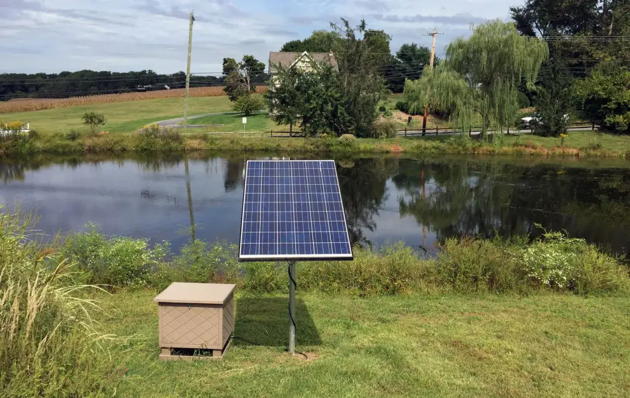 Panneau solaire pr&egrave;s d'un &eacute;tang, solution pour comment oxyg&eacute;ner l'eau sans pompe. Un bo&icirc;tier beige est &agrave; c&ocirc;t&eacute;.