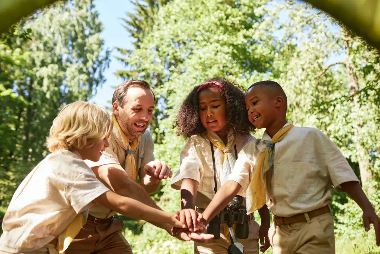 Un animateur et trois enfants en tenue de scout, mains jointes, souriants. Une belle image des stages BAFA en pleine nature.