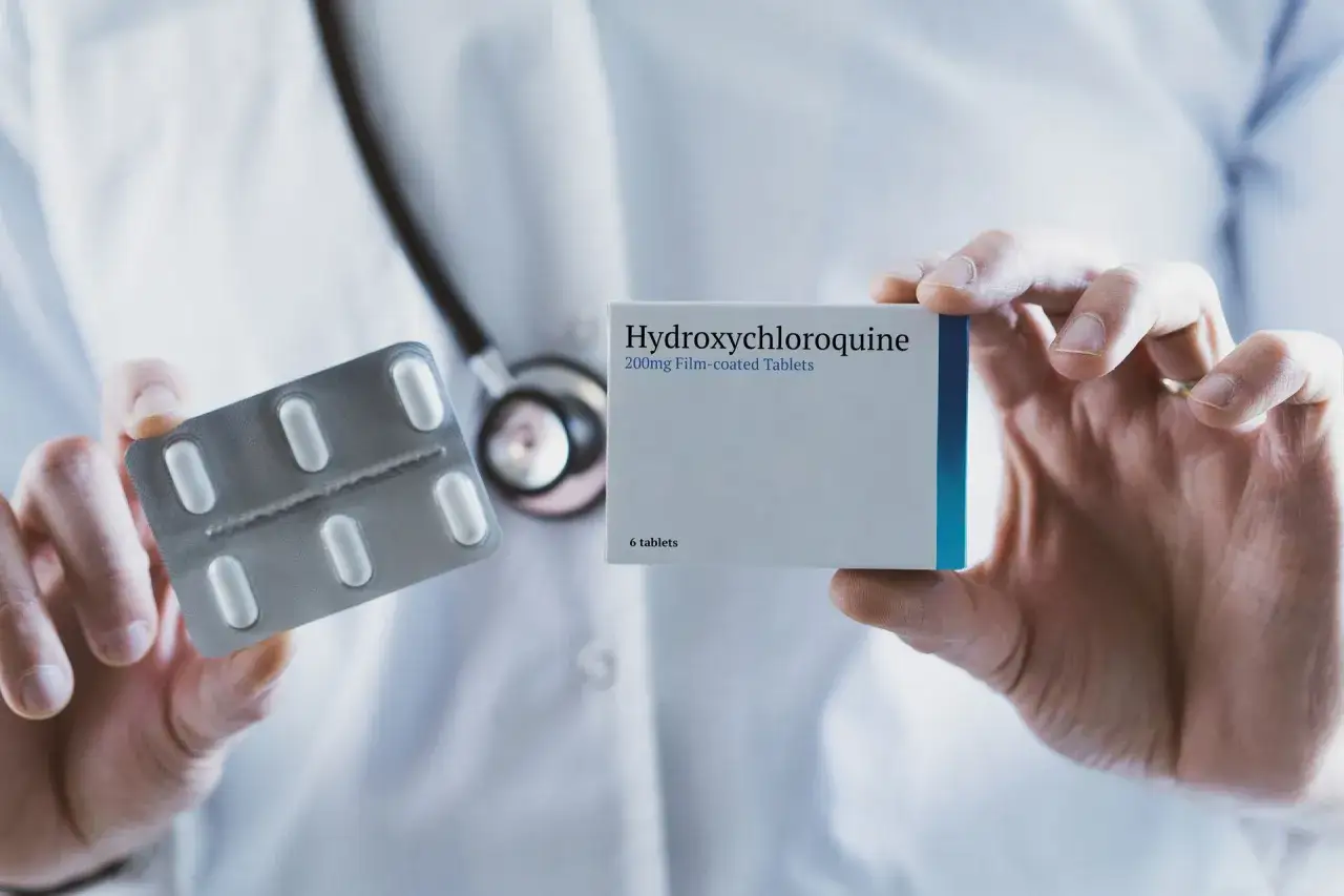 Lekarz prezentuje opakowanie Hydroxychloroquine Adamed i blister z tabletkami.