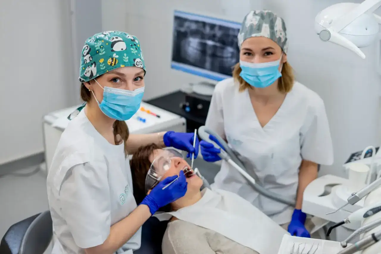 Dwie dentystki w maseczkach i czepkach z pandami przeprowadzają zabieg sanacji zębów u pacjentki.