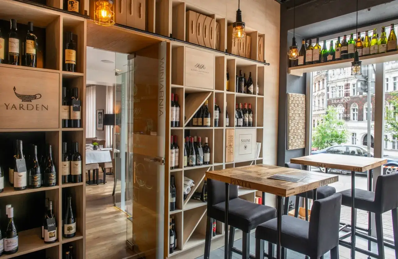 Elegancka piwniczka z winami w restauracji Muga. Drewniane regały pełne butelek, stoły z recyklingu i widok na ulicę.