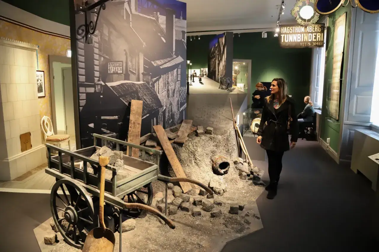 Bes&ouml;kare utforskar en historisk gatumilj&ouml; p&aring; stadsmuseet i Stockholm, med en gammal vagn och byggmaterial.