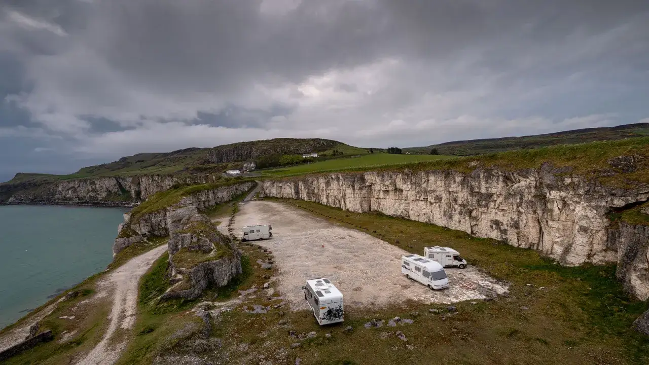 Wohnmobile parken am Rand einer Klippe mit Blick auf das Meer. Ein perfekter Ort für einen Irland Roadtrip unter dramatischem Himmel.
