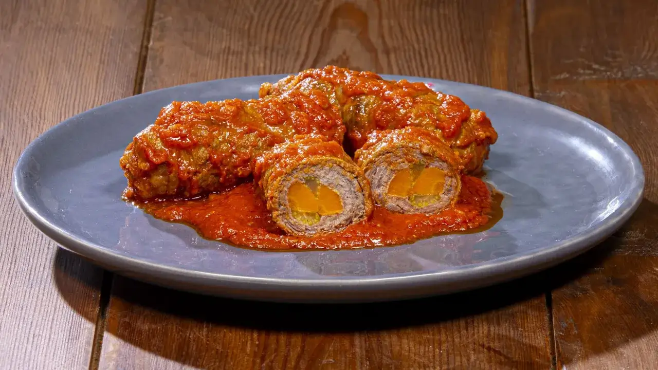 Involtini alla romana succulenti, avvolti in un sugo rosso intenso, con un ripieno dorato visibile in sezione.