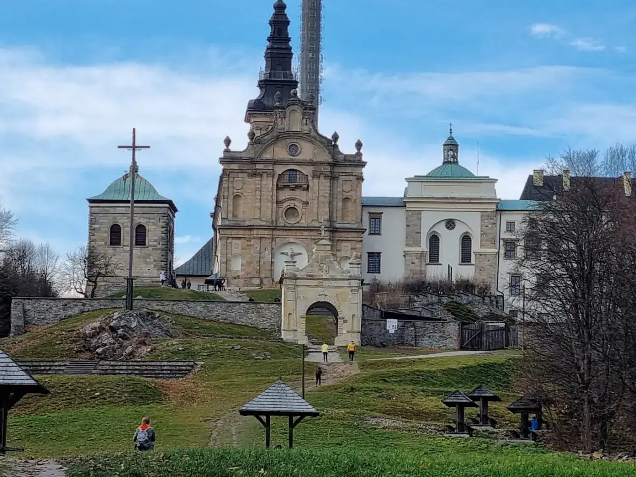 Wzgórze z krzyżem i barokowymi budynkami, przypominające o historii klasztorów w Polsce.