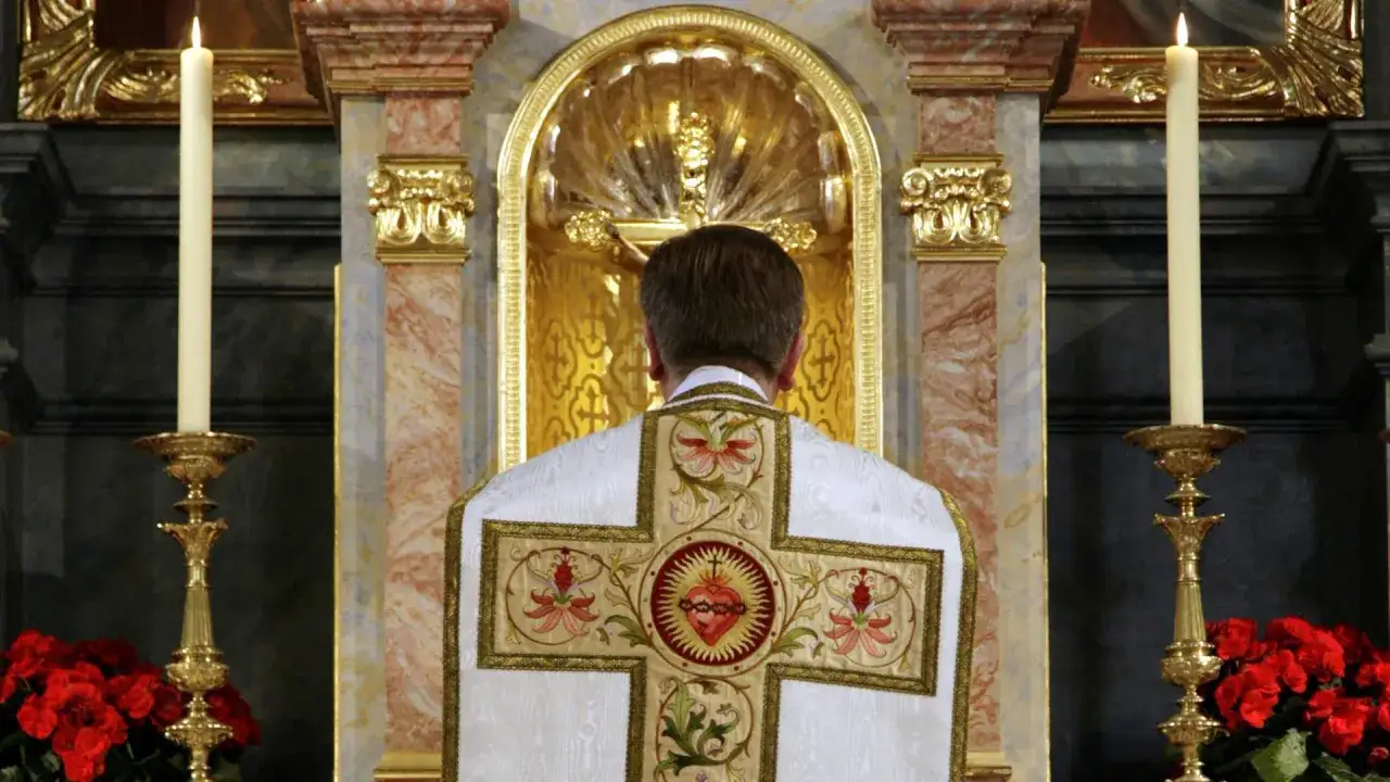 Priester im Messgewand vor goldenem Altar. Die Stickerei auf dem Gewand symbolisiert die Bedeutung von Dogma und Glauben.