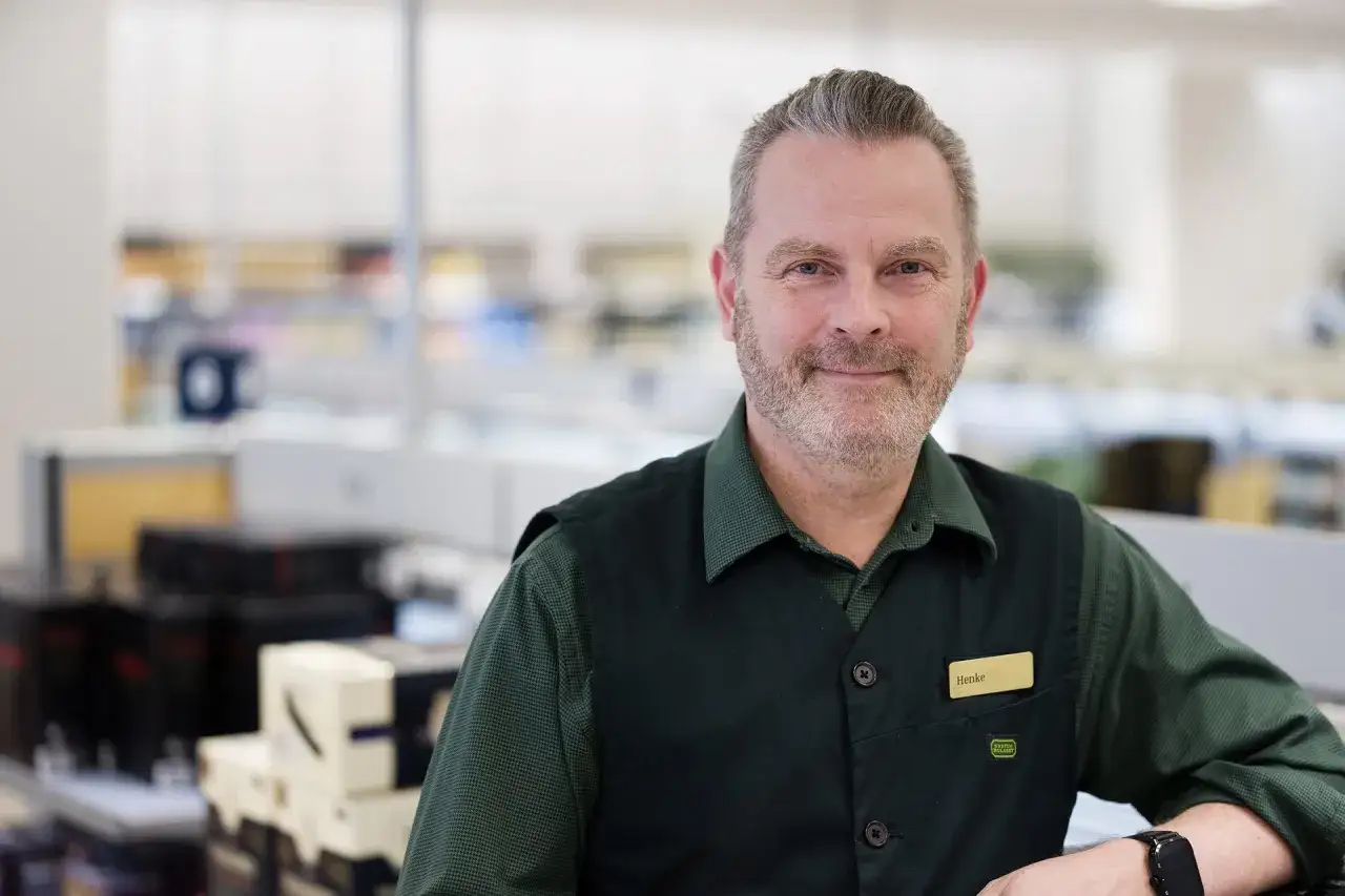 Henke, en vänlig sem specialist, ler mot kameran i en butiksmiljö.