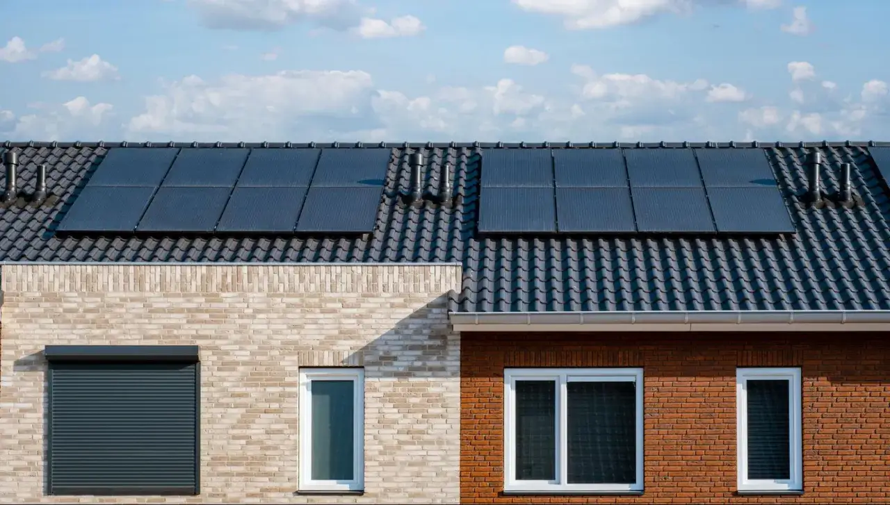 Tejas oscuras con paneles solares. Dos casas adosadas, una de ladrillo claro y otra de ladrillo rojo, con ventanas y persianas. Obtener permisos para instalar placas solares en casa es el primer paso.
