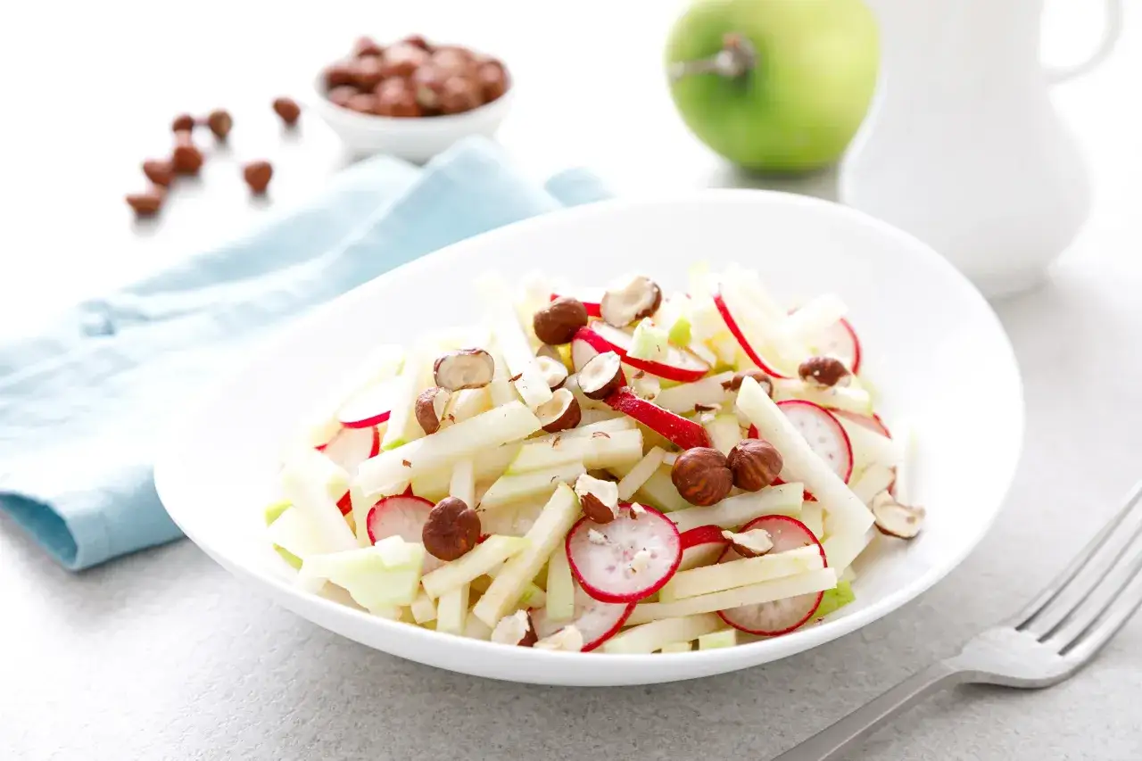 Frischer Kohlrabi Apfel Salat mit Radieschen und Haselnüssen, garniert mit knackigen Nüssen.
