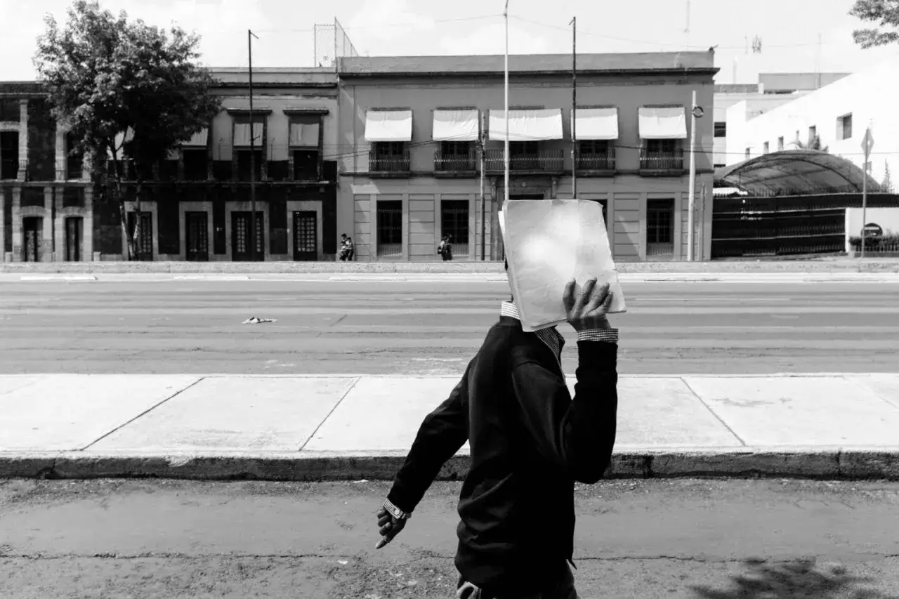 Un uomo con un foglio bianco davanti al viso cammina sul marciapiede. Fotografia di strada.