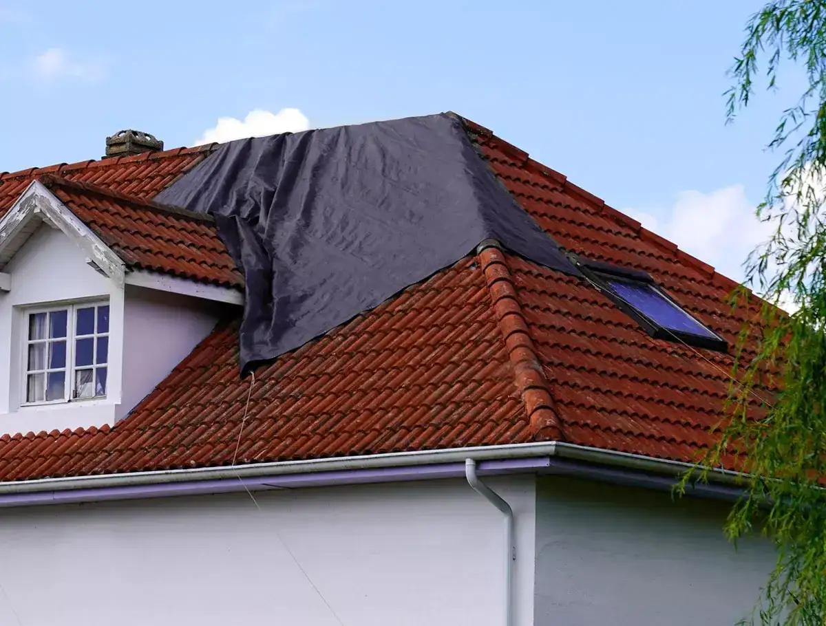 Tymczasowe zabezpieczenie dachu domu przed deszczem, przykryte ciemną plandeką.