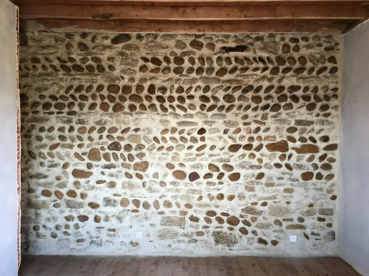 Mur en pierre de rivi&egrave;re avec un mortier clair. La couleur du joint du mur en pierre met en valeur les galets de diff&eacute;rentes tailles et teintes.