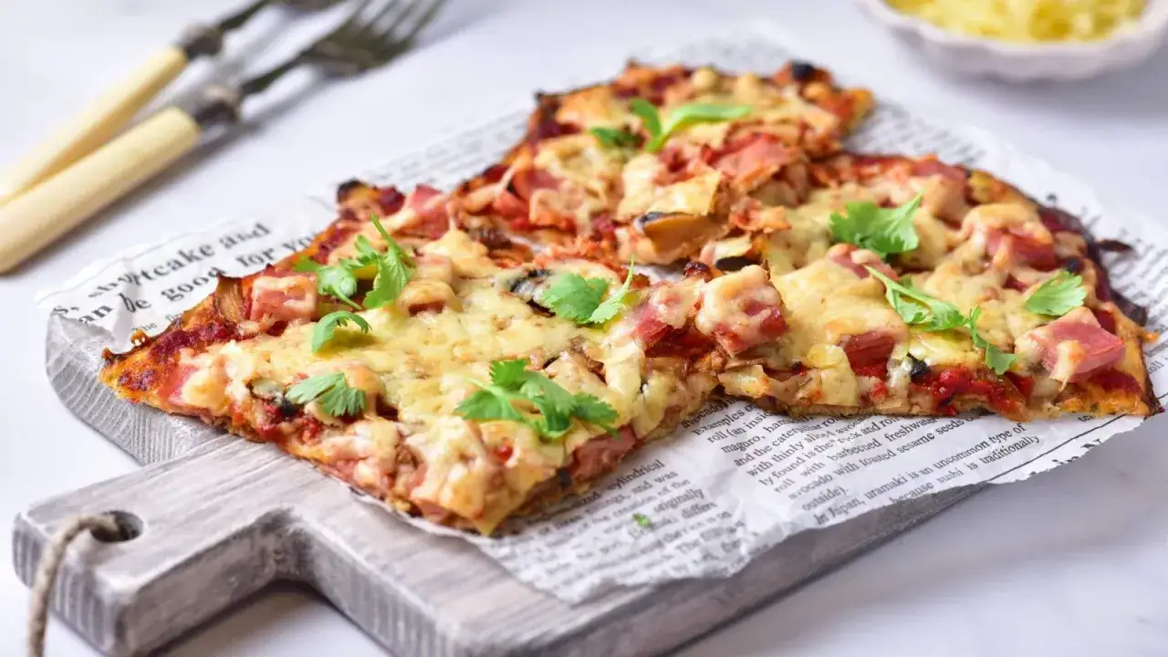 Pyszna pizza na spodzie z kalafiora keto z szynką i serem, udekorowana natką pietruszki.