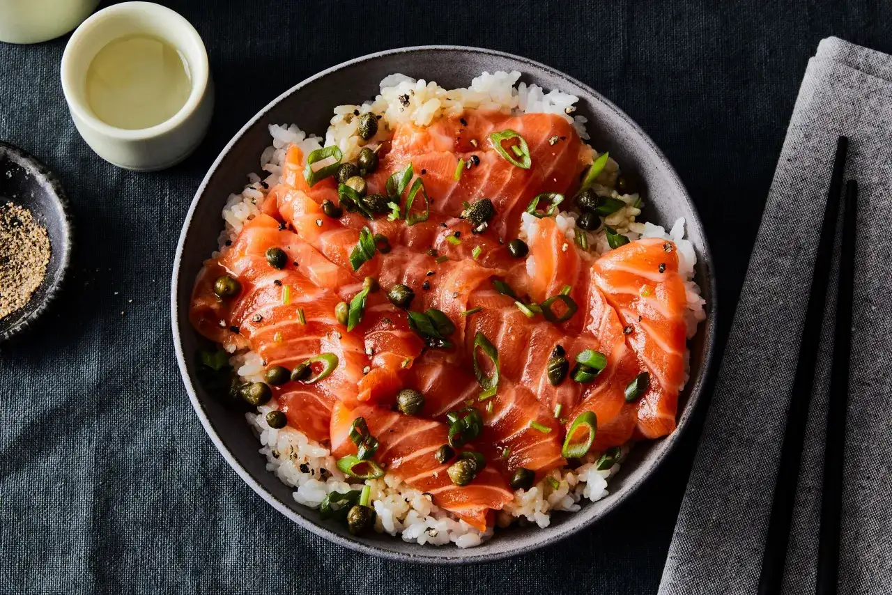 Miseczka ryżu z łososiem, kaparami i szczypiorkiem, polana delikatną zalewą do sushi.