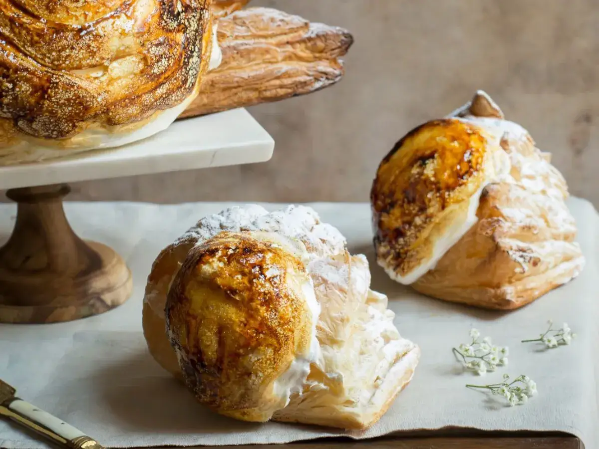 Dos deliciosos panes de Calatrava, cubiertos de azúcar glas y caramelo tostado, reposan sobre papel de horno.