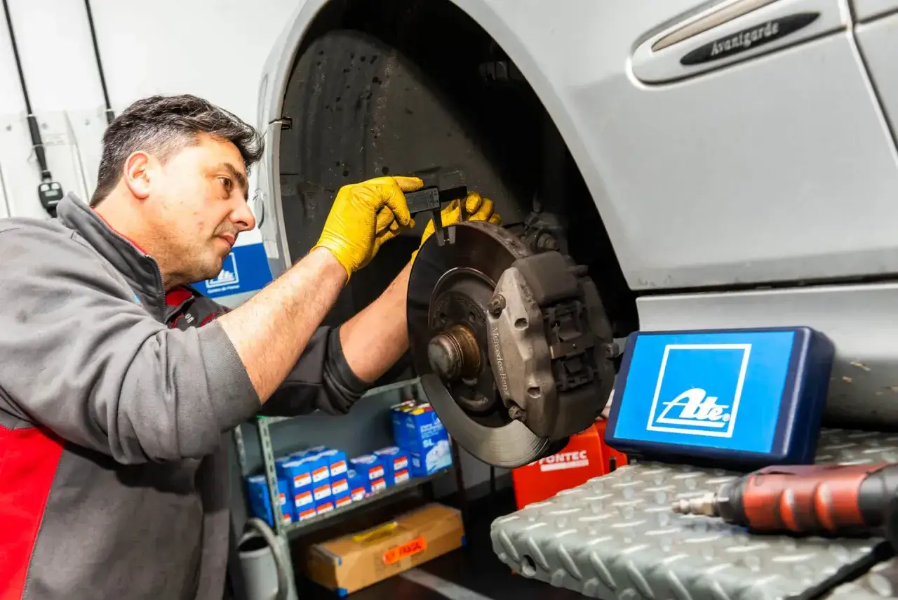 Mecánico revisa frenos para el mantenimiento anual del coche. Usa un calibrador para medir el disco.