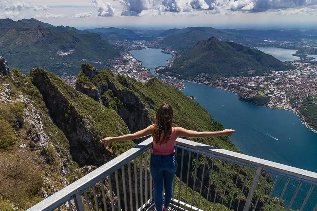 Una ragazza con le braccia aperte ammira il panorama mozzafiato durante una passeggiata al Pian dei Resinelli, con il lago e le montagne sullo sfondo.