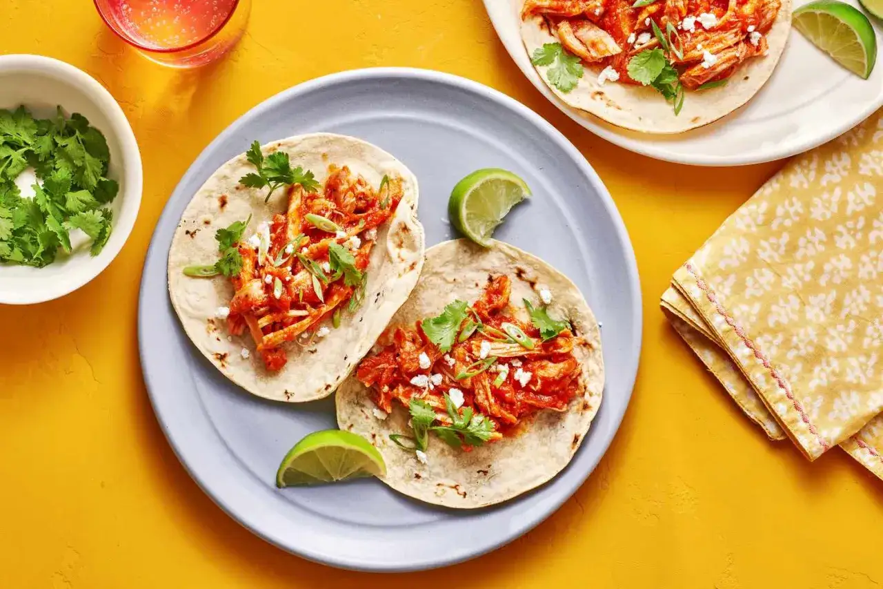 Två läckra kycklingtinga-tacos med färsk koriander och lime på en ljusblå tallrik.