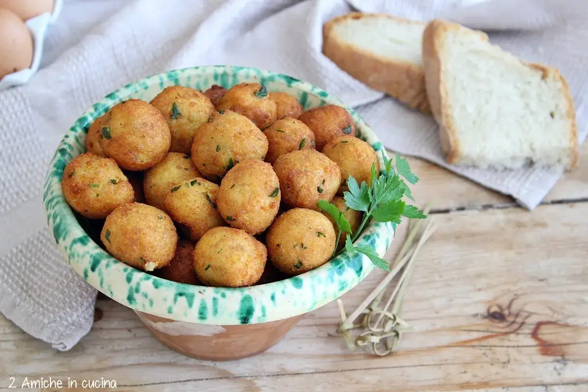 Ciotola piena di dorate polpette di pane, guarnite con prezzemolo fresco. Sullo sfondo, fette di pane e uova.