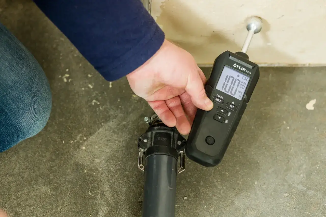 Miernik wilgoci FLIR MR60 pokazuje 100% wilgoci na ścianie, wskazując problem.