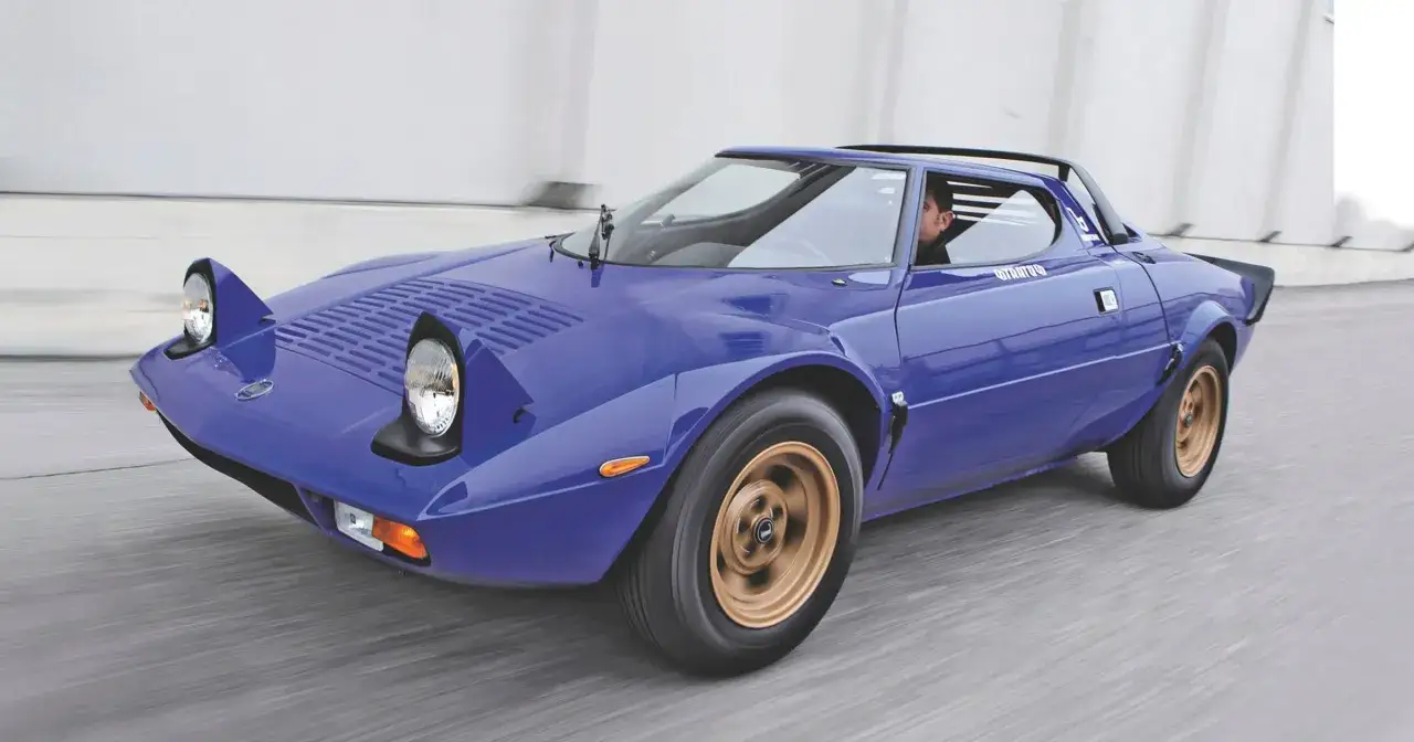 Niebieski Lancia Stratos z wysuwanymi światłami pędzi po drodze, kierowca w środku.