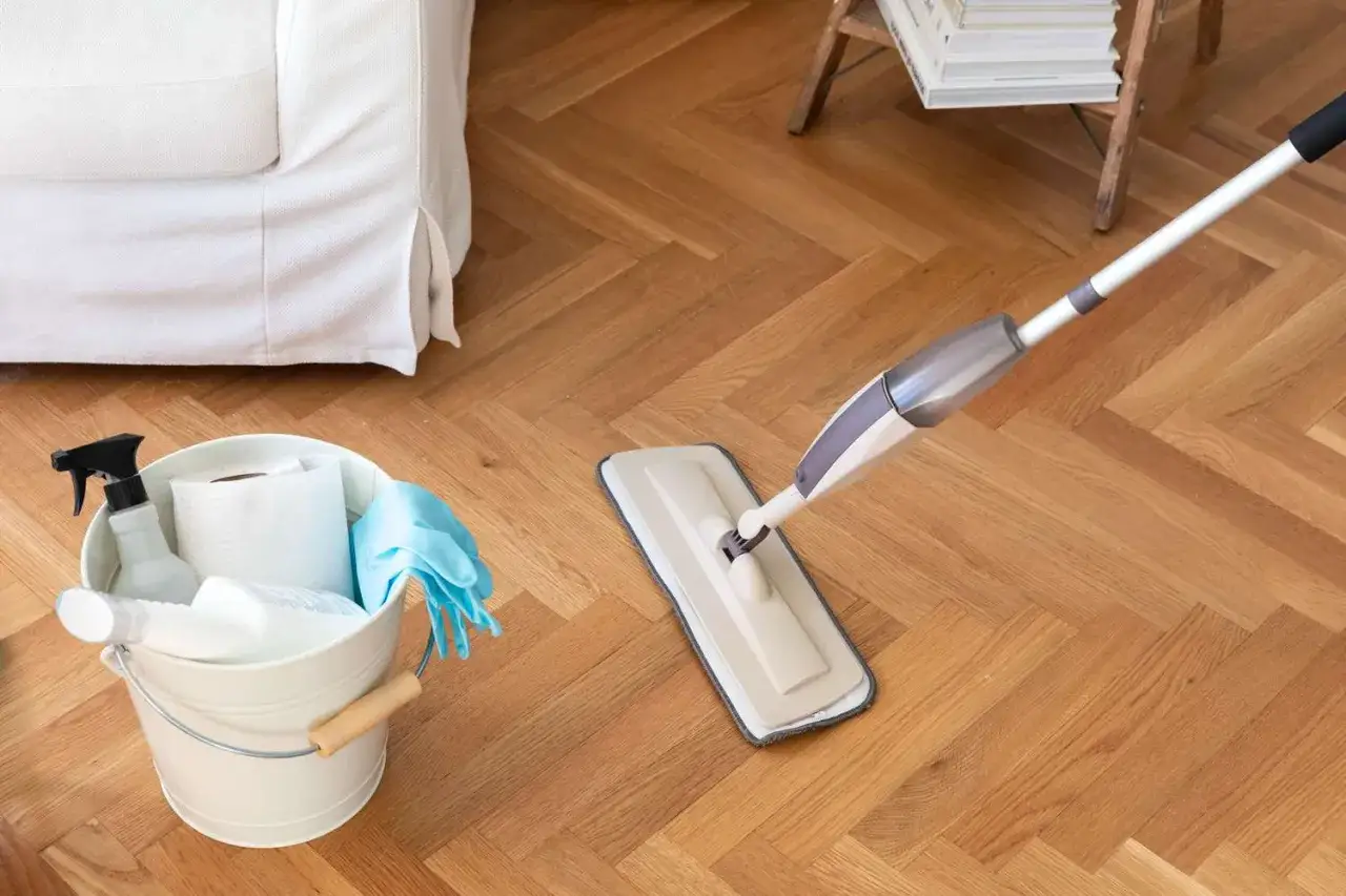 Nettoyer sol vinyle vinaigre blanc : un seau de produits m&eacute;nagers et une serpilli&egrave;re &agrave; pulv&eacute;risation sur un parquet en chevrons.