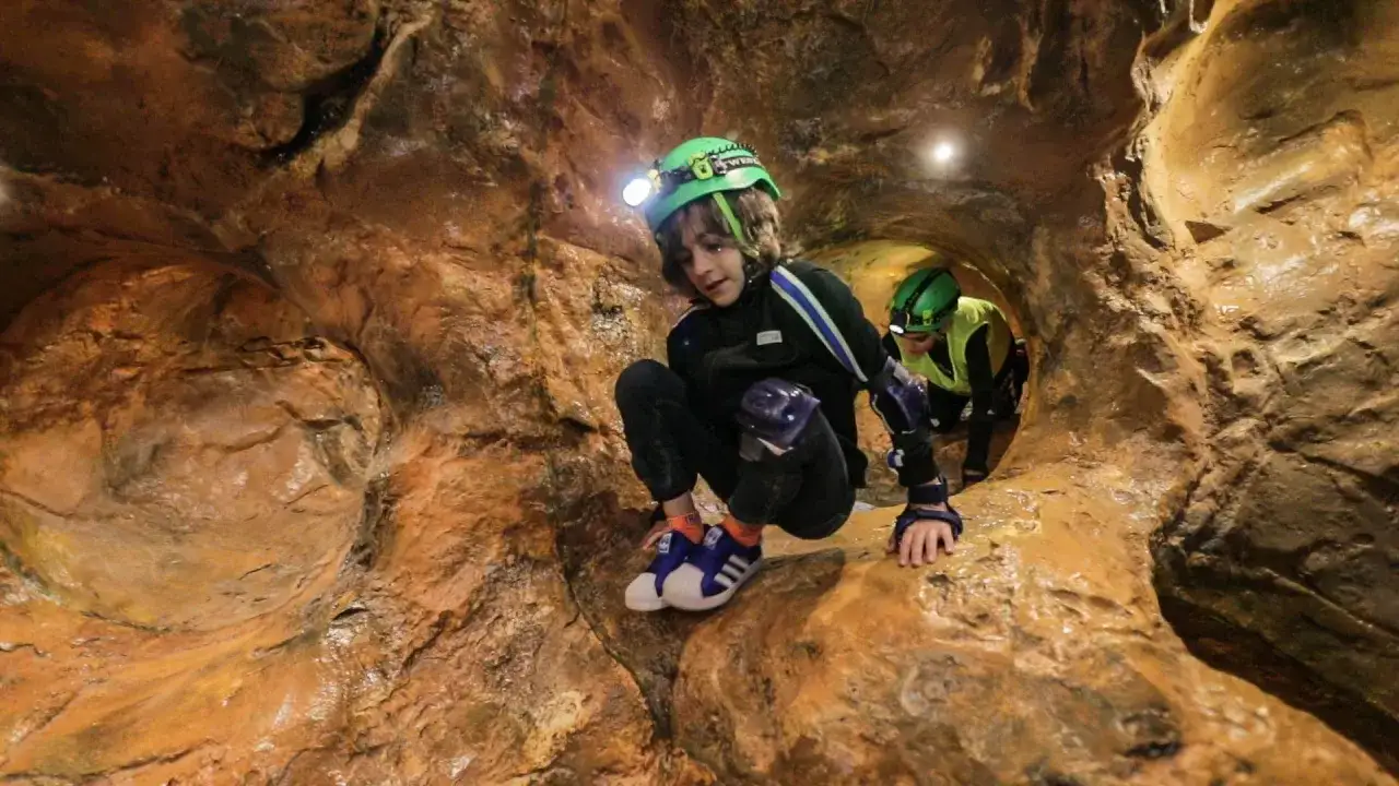 Dzieci w kaskach z czołówkami eksplorują jaskinię. To właśnie jest speleologia – fascynująca przygoda w podziemiach.