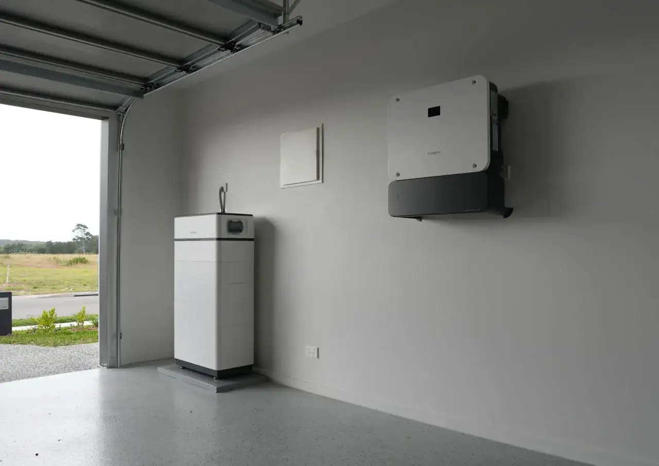 En vit batterienhet och en v&auml;ggmonterad Sungrow v&auml;xelriktare i ett garage.