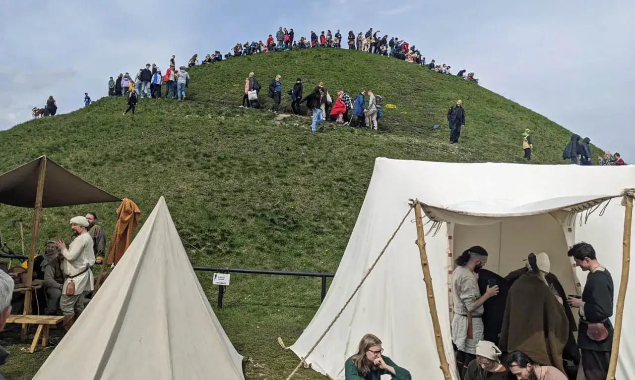 Ludzie wchodzą na zielony kopiec Kraka, a pod nim rozstawiono namioty w stylu historycznym.