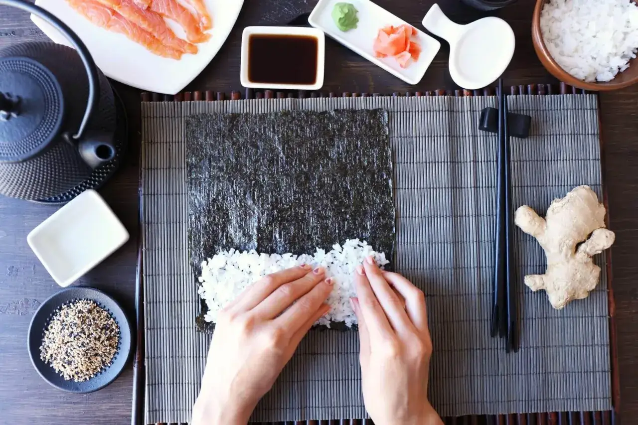 Przygotowanie zaprawy do sushi na 500g ryżu. Na macie bambusowej układany jest ryż na nori. Obok łosoś, sos sojowy, imbir, wasabi.