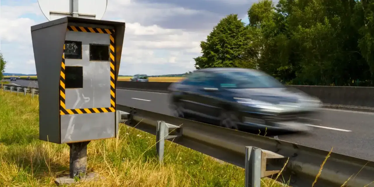 Un radar de bord de route, avec ses bandes jaunes et noires, surveille le trafic. Une voiture passe en flou sur l'autoroute. Ces photos des différents radars rappellent la vigilance.