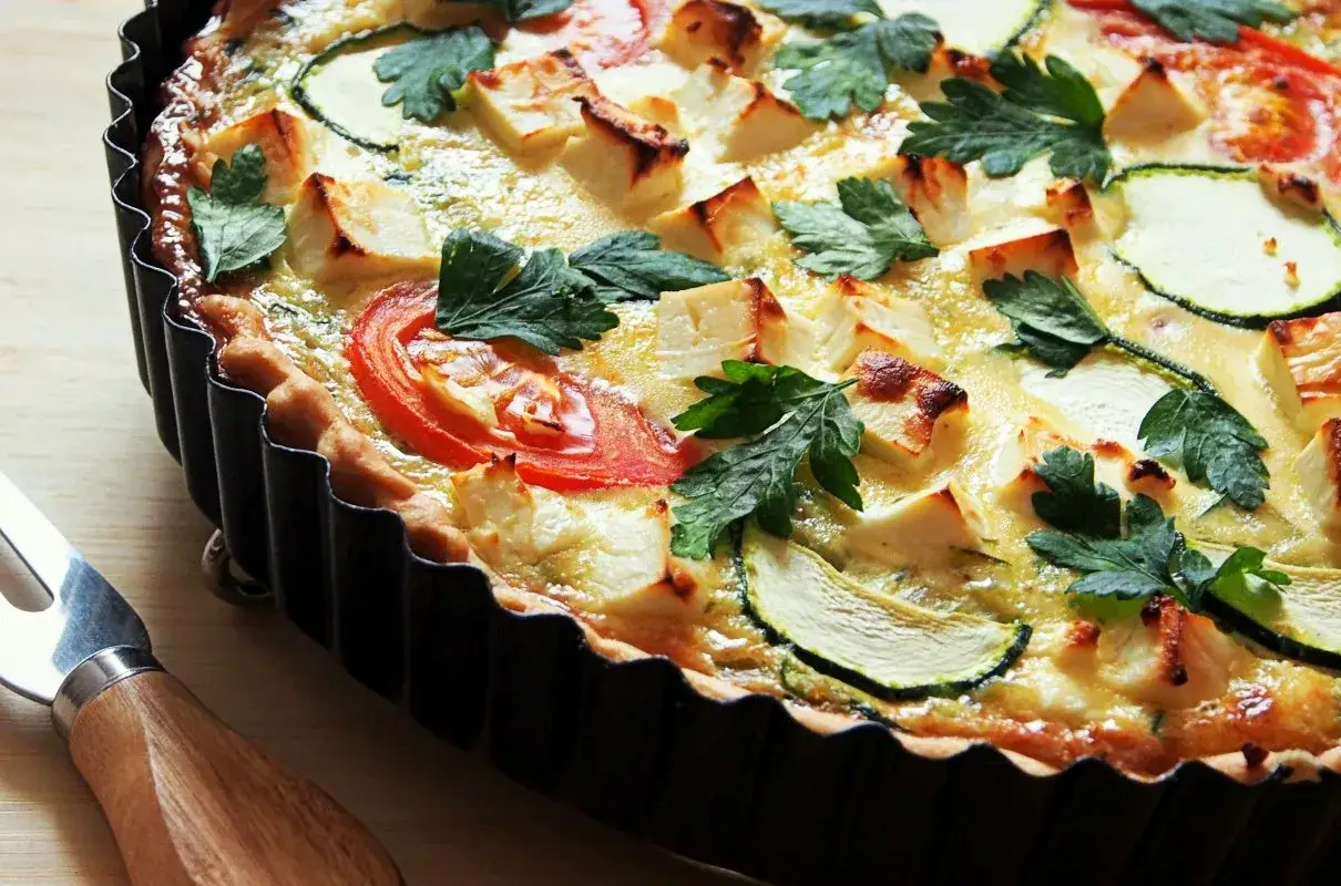 Pyszna tarta na słono z cukinią, pomidorami i serem feta, udekorowana natką pietruszki. Idealna na lekki obiad lub kolację.