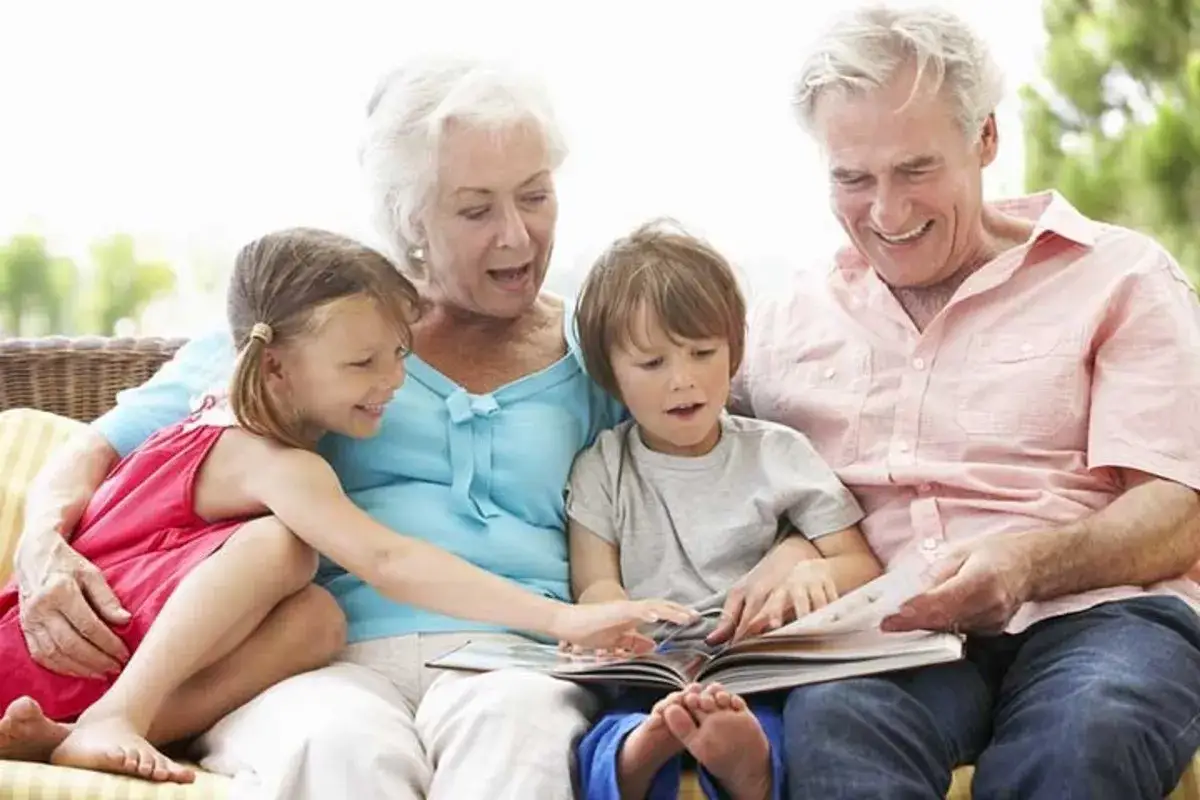 Los abuelos son un tesoro. Un abuelo lee un libro a sus nietos, mientras la abuela sonr&iacute;e.