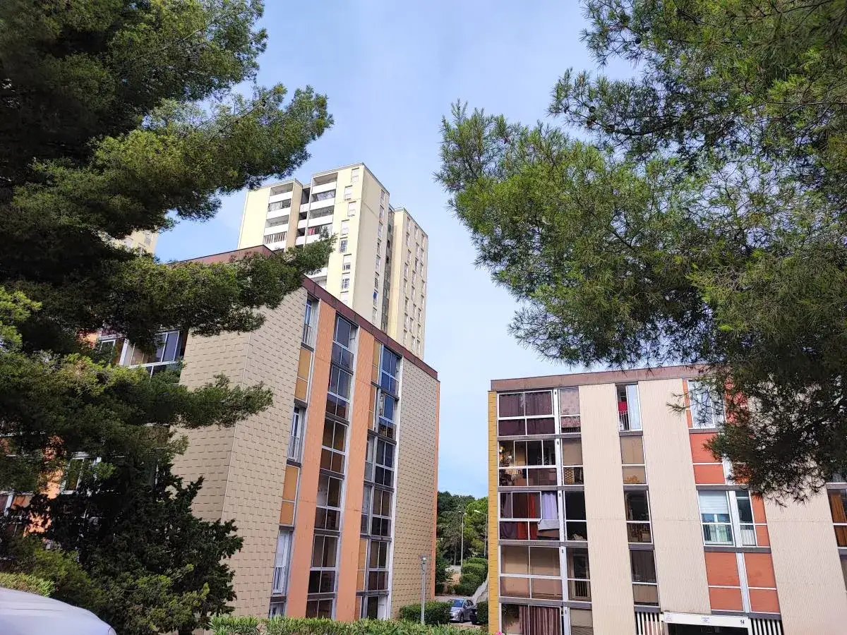 Immeubles résidentiels sous un ciel bleu, entourés de pins. Un modèle pétition locataires pourrait être signé ici.